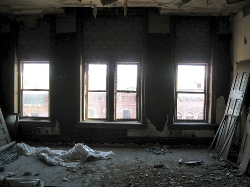 Upstairs front room before: dark, peeling walls and debris under the street-facing windows
