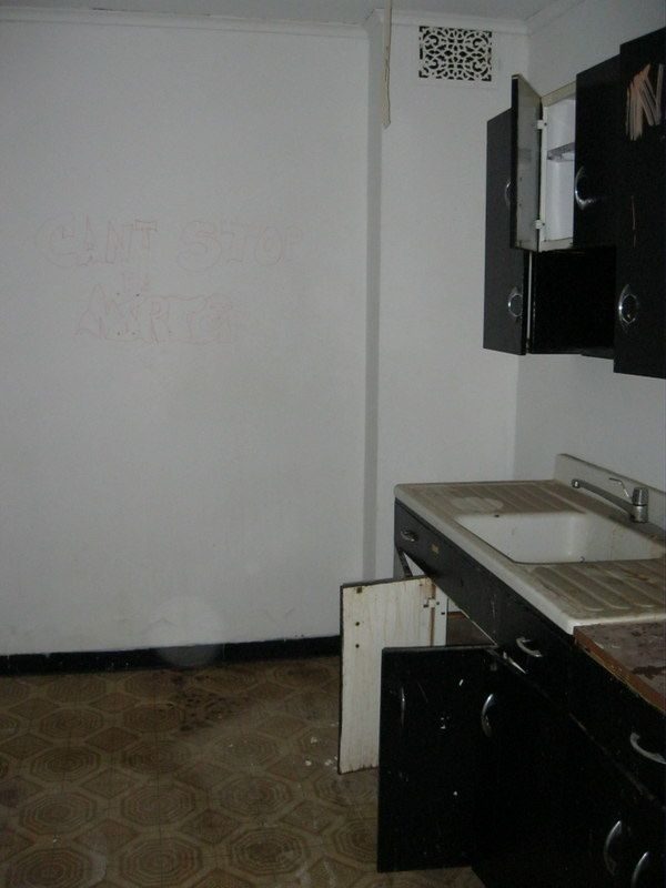 Old kitchen before: broken cabinets, graffiti, and worn flooring