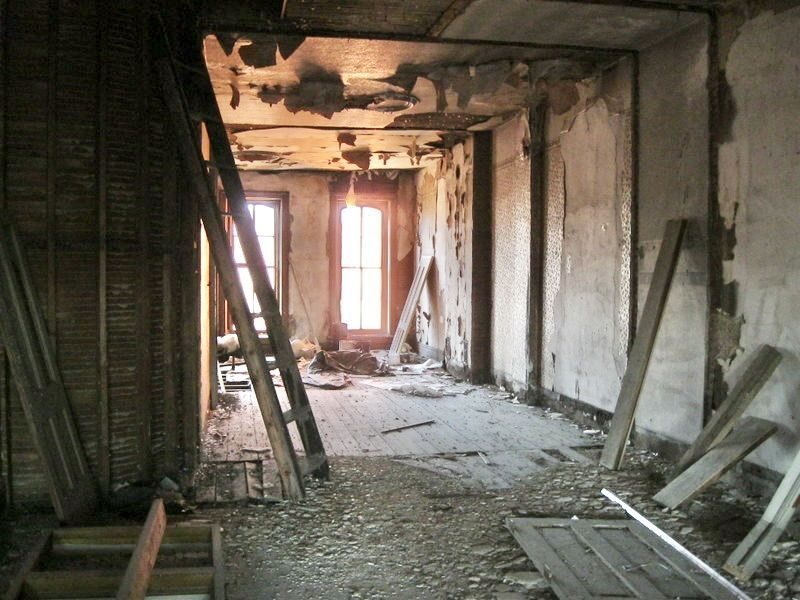 Upstairs hallway before: fire-damaged ceiling, stripped walls, and a ladder